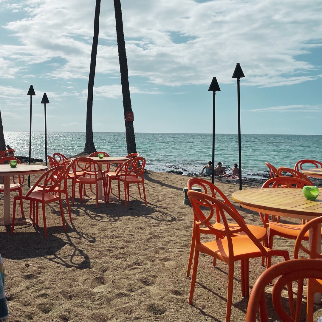 Coral-colored chairs at a beachfront caf&eacute; under palms on Hawai'i Island