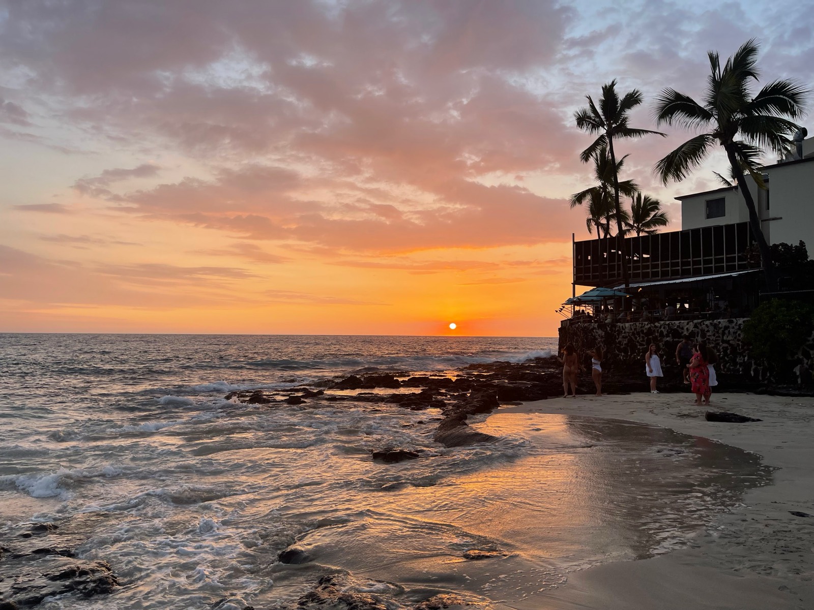 Sunset over the ocean at a Kona beach, palms and lava rock in silhouette