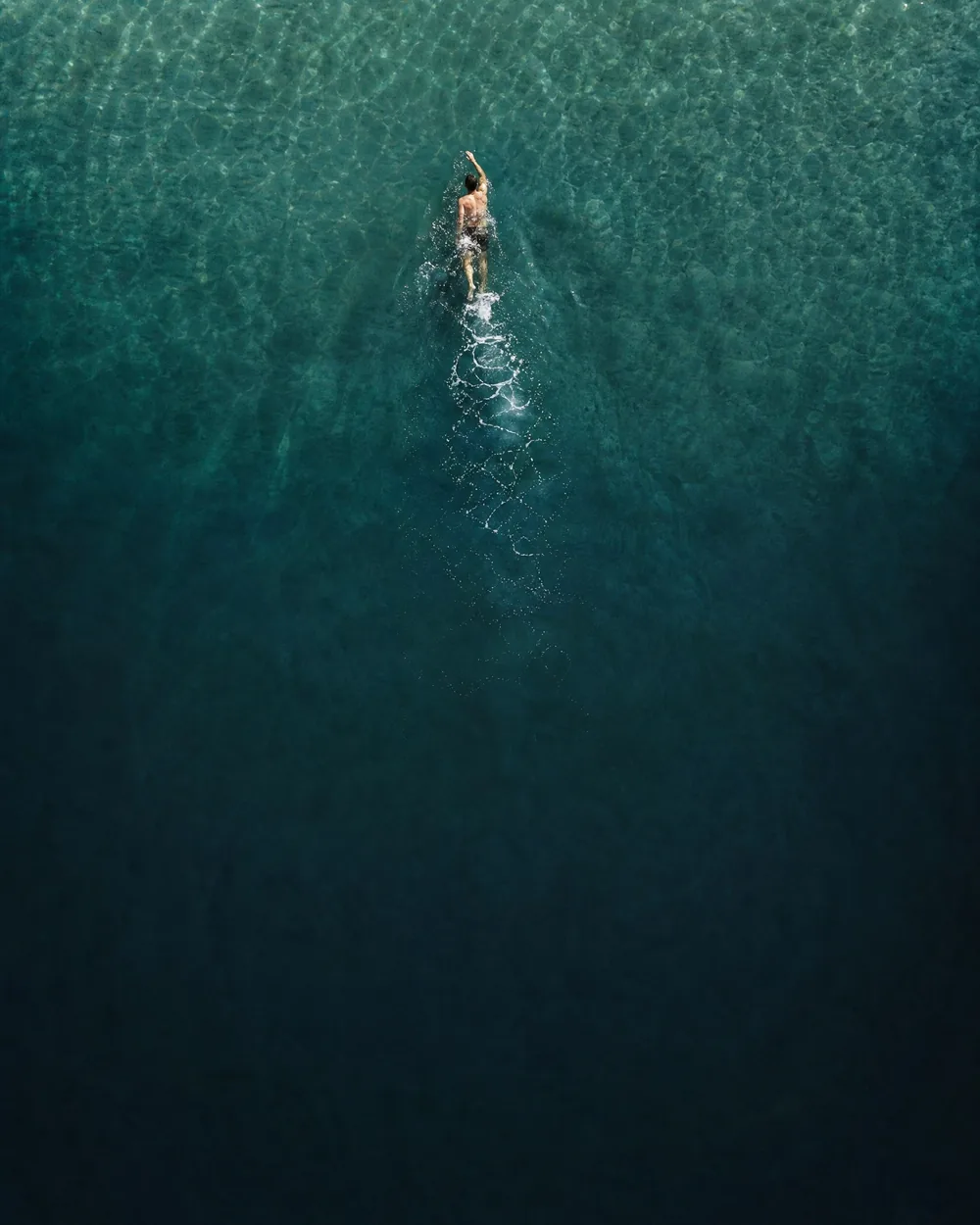 One swimmer seen from above, small in a wide field of clear turquoise water